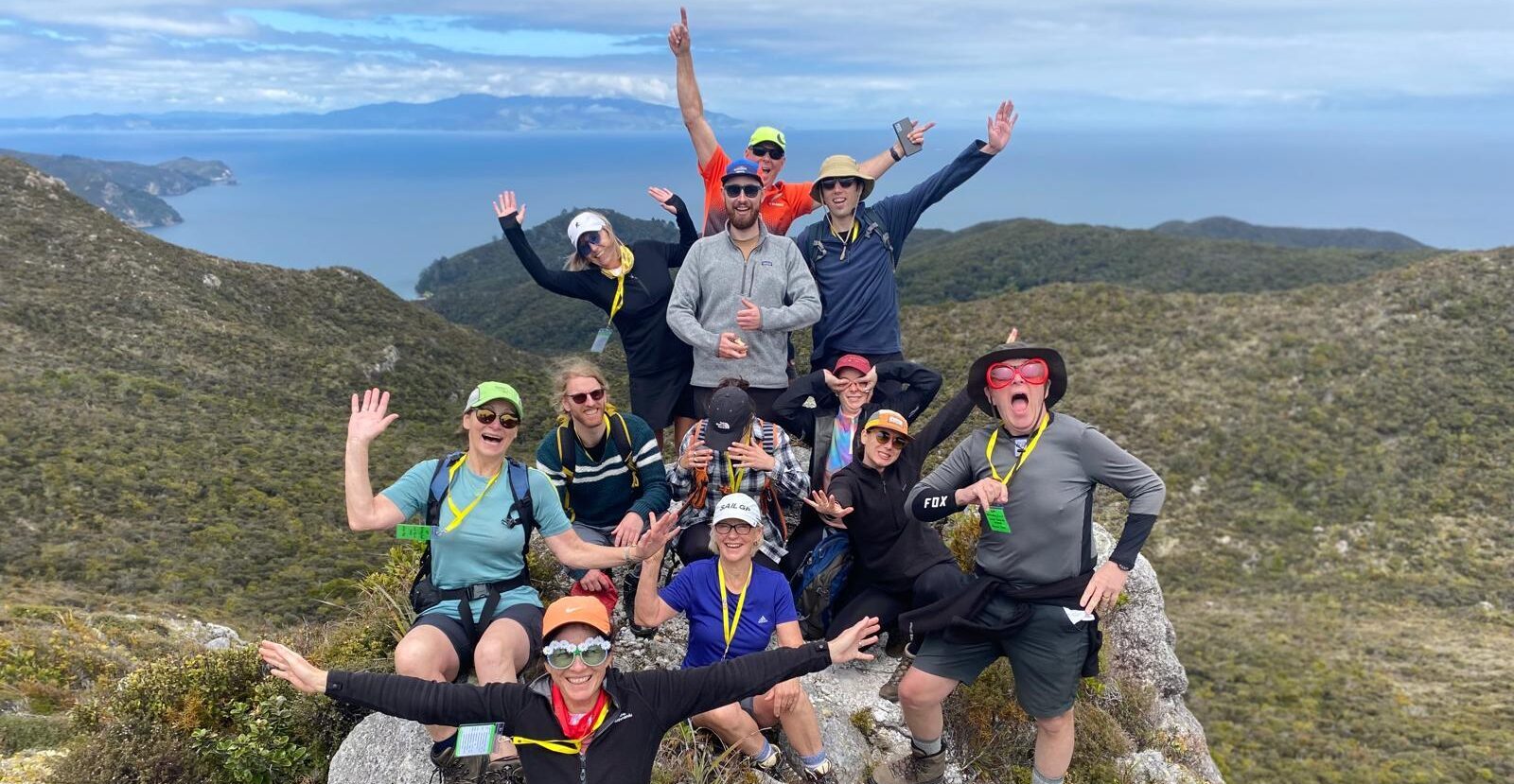 A group of hikers stand triumphantly atop the Te Ahumata/Whitecliffs summit on Aotea/Great Barrier Island, on a guided walk in New Zealand