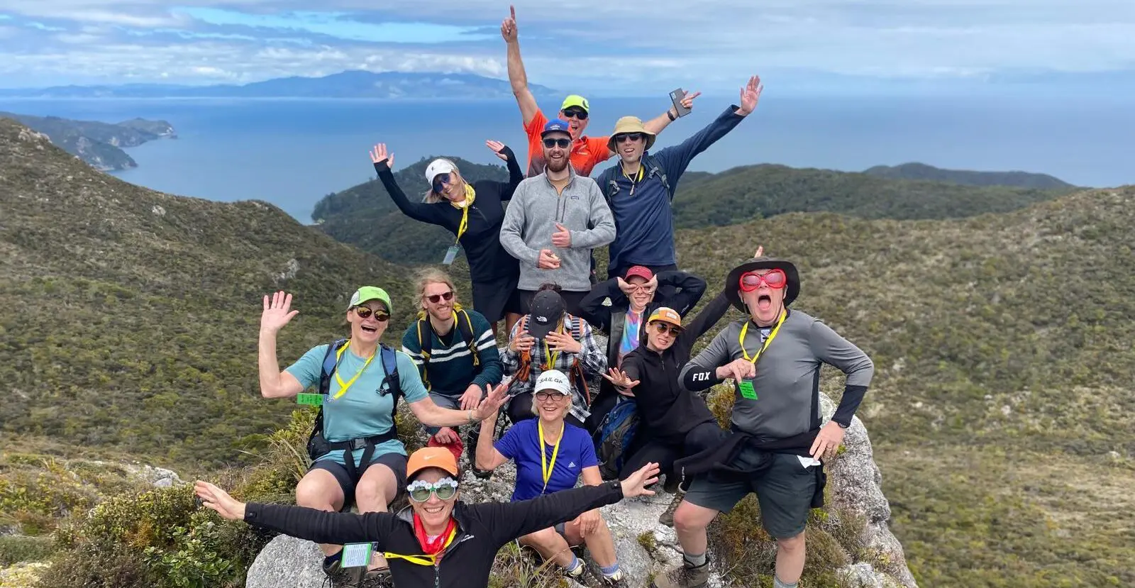 A group of hikers stand triumphantly atop the Te Ahumata/Whitecliffs summit on Aotea/Great Barrier Island, on a guided walk in New Zealand