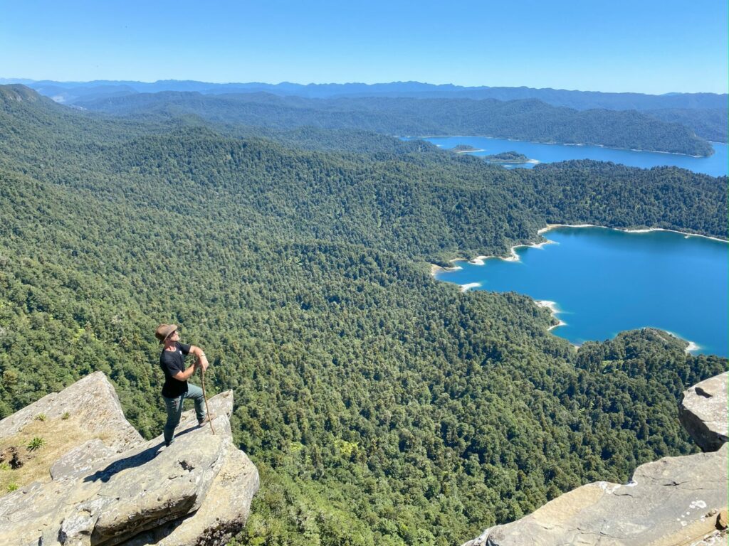 A hiker stands on a rocky outcrop high above Lake Waikaremoana, Te Urewera, North Island, New Zealand