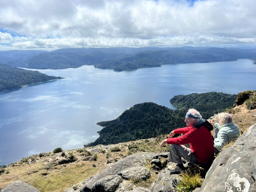 A hiker sits on Bald Knob a high rocky precipice above Lake Waikaremoana, Te Urewera, New Zealand