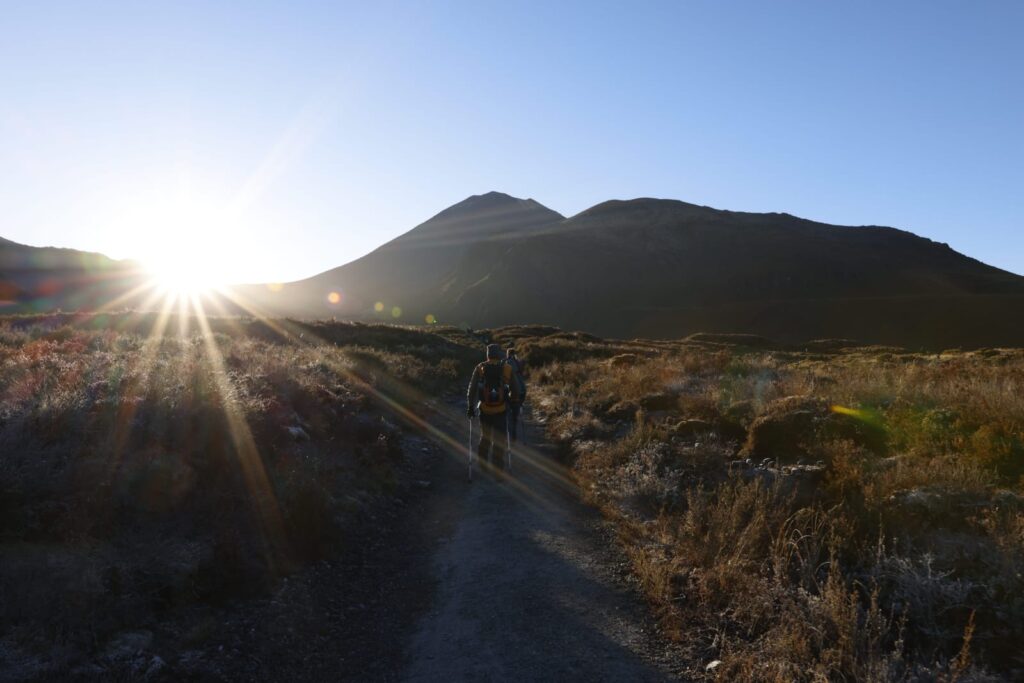 A pair of hikers start out on the Tongariro Alpine Crossing as the sun rises above the mountain peaks ahead of them