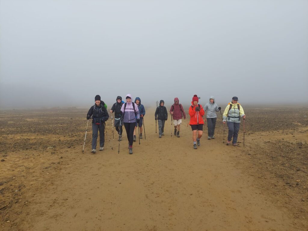 A group of hikers cross South Cirque surrounded by cloud and mist forming a solid grey backdrop on the Tongariro Alpine Crossing