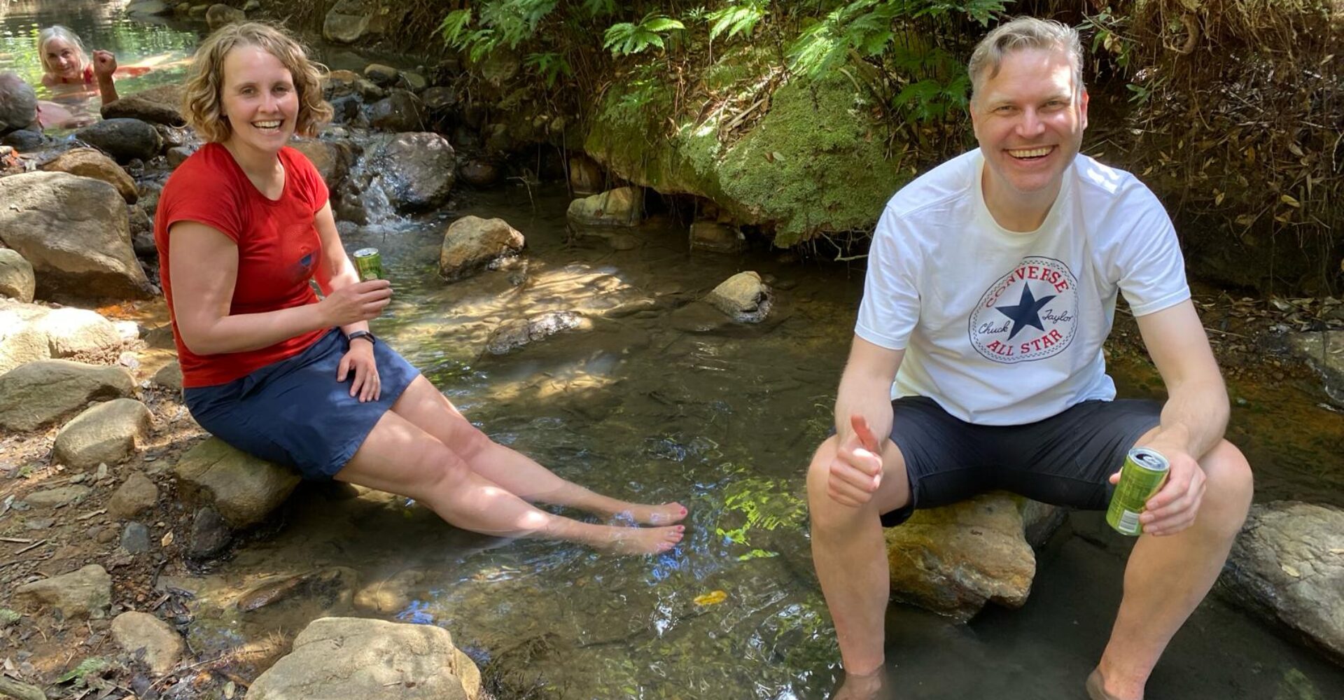 Two hikers soaking their feet in Kaitoke Hot Springs at the end of the Aotea Track on Great Barrier Island near Auckland New Zealand, as part of a guided hiking tour with Walking Legends